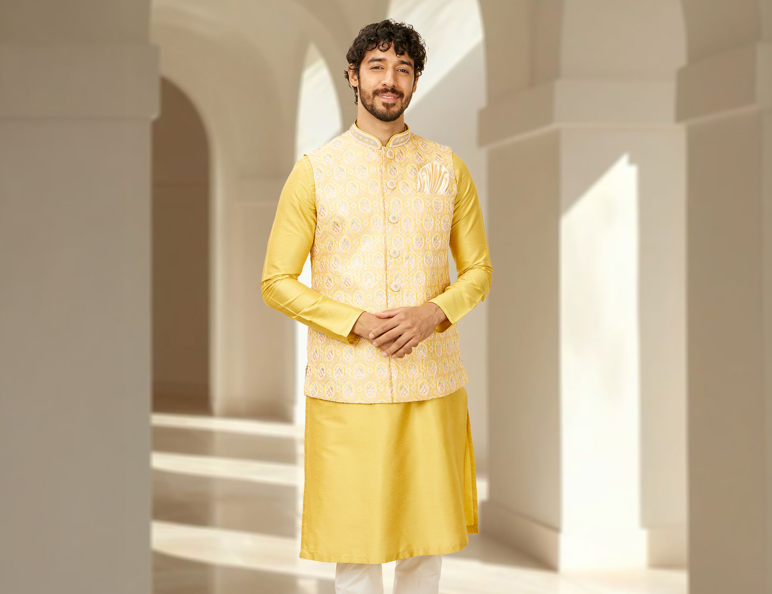 A man dressed in a golden jacket over a yellow kurta pajama, styled for a traditional wedding event.